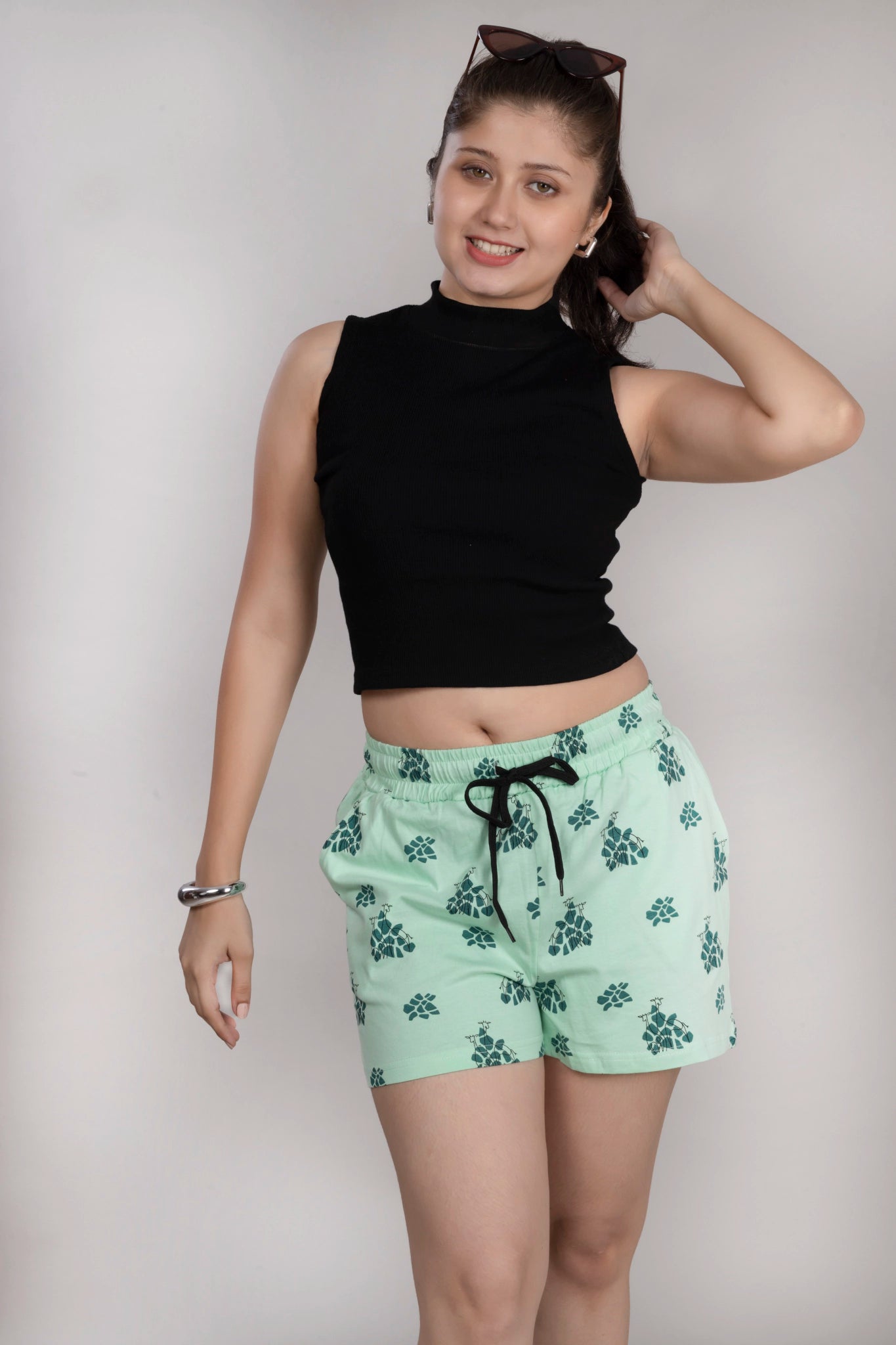 Woman wearing a black crop top and green shorts with a floral pattern on a plain background